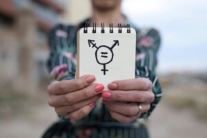 A closeup of a young woman outdoors showing a notepad in front of her with a transgender symbol drawn in it