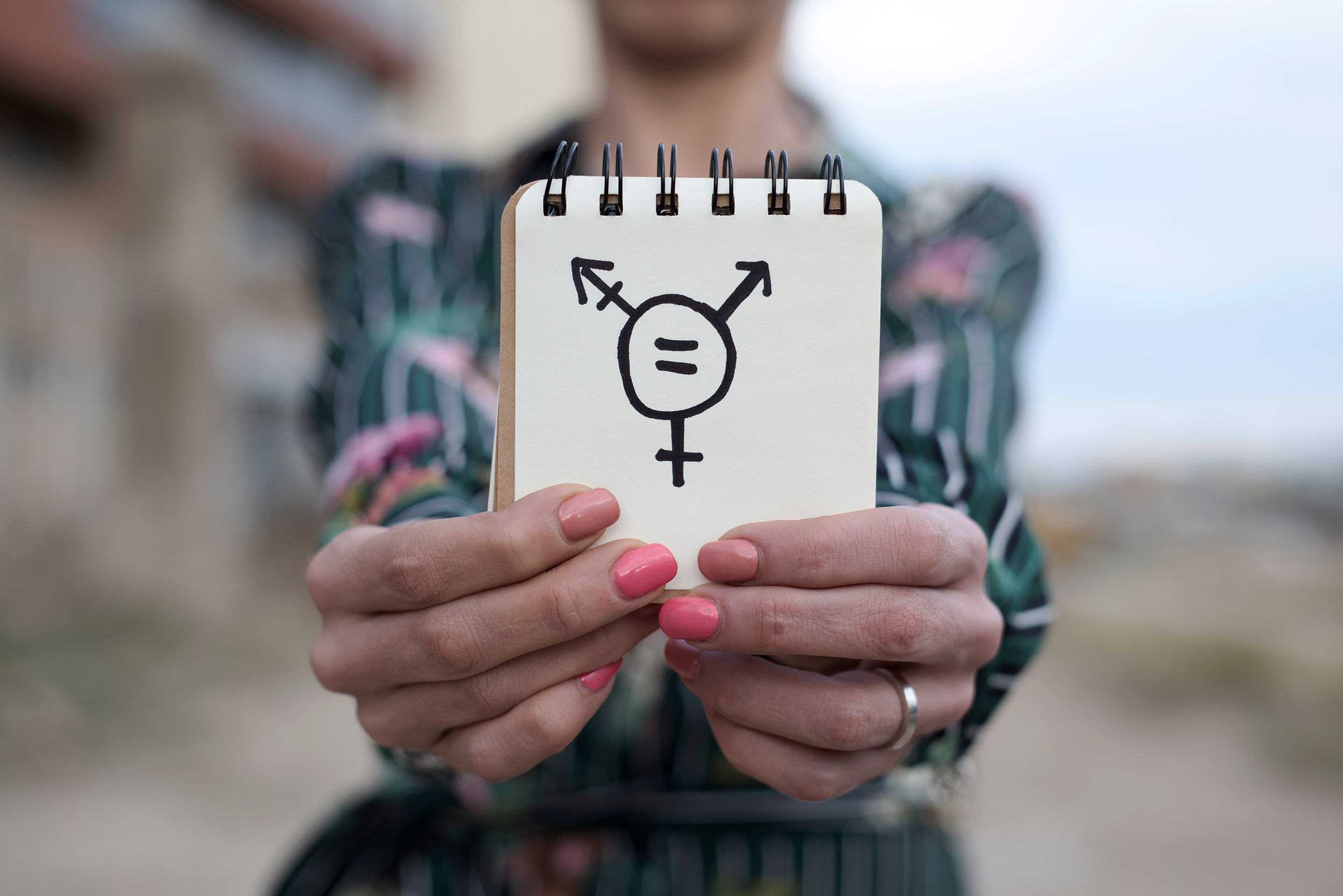 A closeup of a young woman outdoors showing a notepad in front of her with a transgender symbol drawn in it
